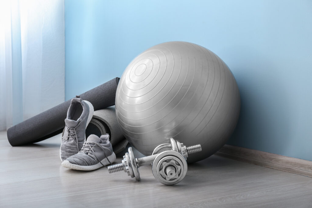 Silberner Gymnastikball, Hanteln, Matte und Sportschuhe für ein ganzheitliches Gesundheitstraining – Krafttraining und Aufbautraining bei Dodo Stehlo in Pfäffikon SZ.